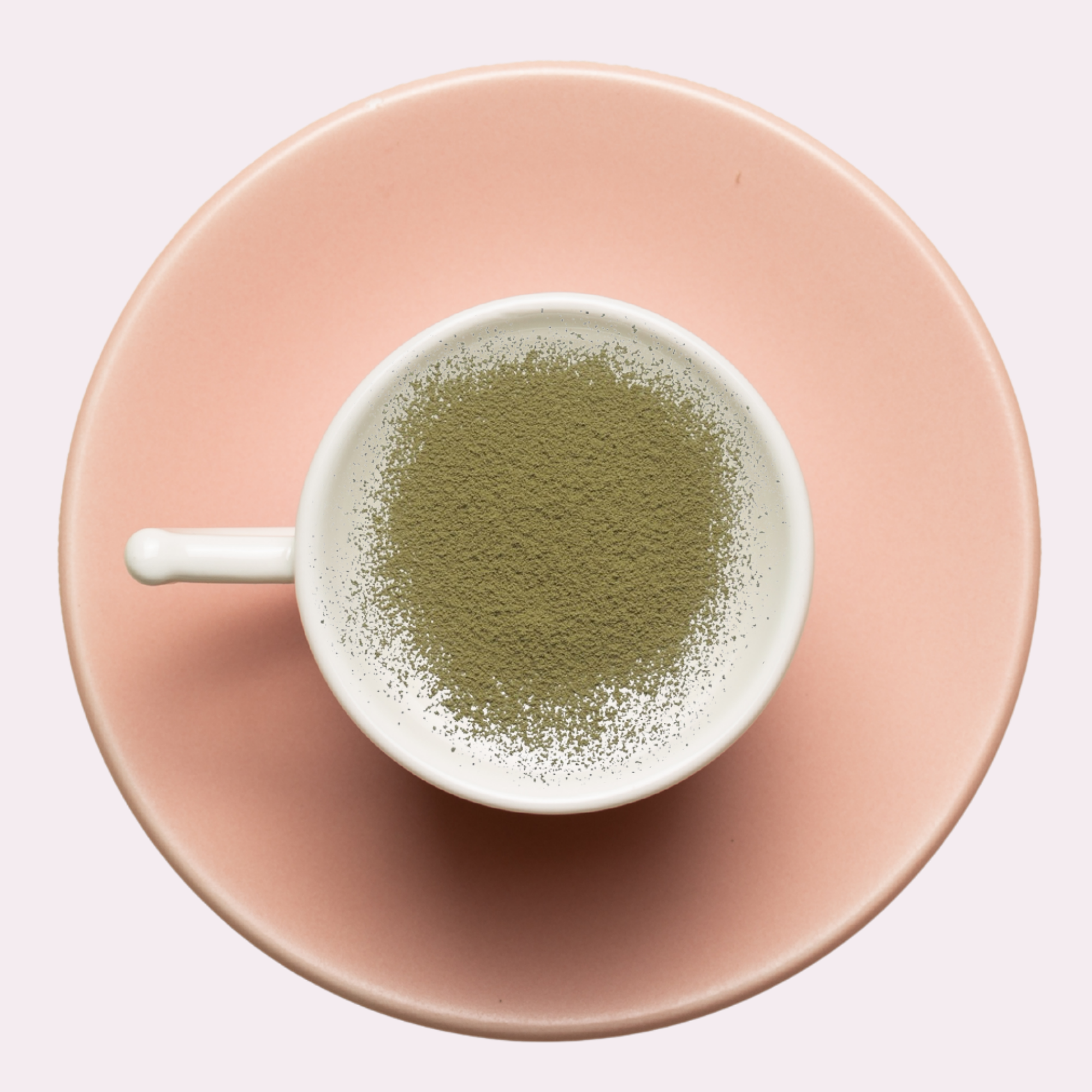 White cup with green powder on a pink saucer against a light pink background